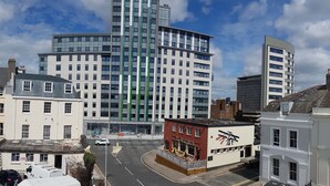 A city street with modern and traditional buildings, including a prominent curved glass building and a red building with a sign. - Quirky Coach House on Plymouth Hoe (Plymouth)