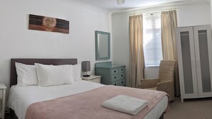 A hotel room with a bed, a dresser, a chair, a mirror, and a window with curtains. - Quirky Coach House on Plymouth Hoe (Plymouth)