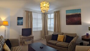 A living room with a checkered sofa, a television on a stand, a small table, and a lamp. - Quirky Coach House on Plymouth Hoe (Plymouth)