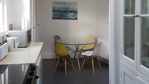 A compact kitchen with a glass table and chairs, a painting on the wall, and white cabinetry. - Quirky Coach House on Plymouth Hoe (Plymouth)