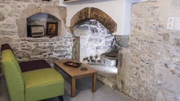 A stone-walled room with a fireplace, a green armchair, and a wooden table with a decorative bowl.