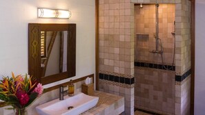 Une salle de bain avec un lavabo blanc, un miroir et un espace douche dont les murs et le sol sont recouverts de carrelage.