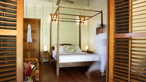 Une chambre dotée d’un lit à baldaquin, de planchers en bois, d’un ventilateur de plafond et d’une porte en bois avec des stores.