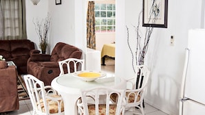 Un salon avec un canapé marron, une table à manger blanche avec des chaises, et un réfrigérateur blanc.