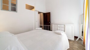 A bedroom with a large bed, a white dresser, a wooden door, and a small window. - Apartment in historical residence in the center of Finalborgo (Finale Ligure)