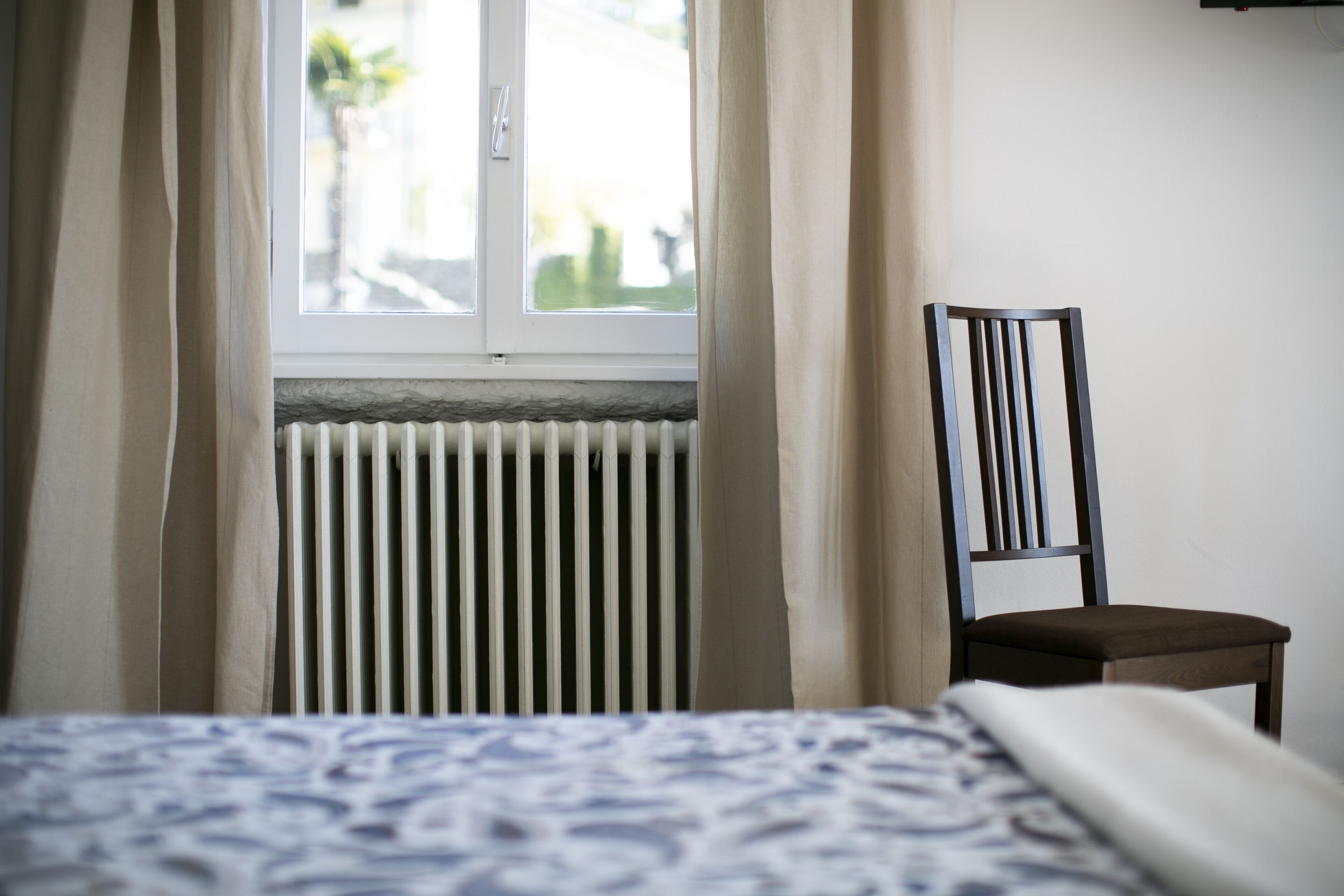 Une chambre à coucher avec un lit, une chaise, une fenêtre avec des rideaux et un radiateur.