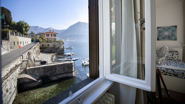 A room with a view of a harbor, boats, and mountains.