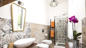 A bathroom with a large vessel sink, a toilet, a shower, and a mirror with a decorative frame.