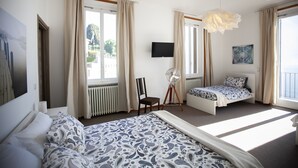 A bedroom with a large bed, a smaller bed, a chair, a TV, and a fan.