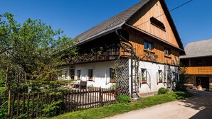 Une maison en bois à deux étages, avec un toit en pente, une clôture en bois et un jardin agrémenté de plantes en pot.