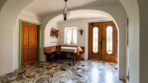 Une pièce avec un sol carrelé, une porte en bois, une table avec des chaises et une fenêtre donnant sur un paysage agréable.