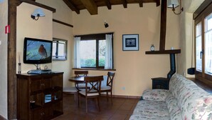 Una sala de estar acogedora con un mueble bajo para el televisor de madera, una mesa de comedor con sillas, un sofá floral y una ventana con cortinas.