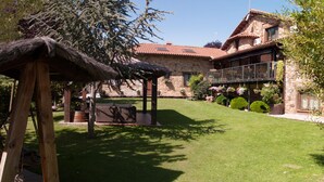 Un edificio de piedra con techo de tejas rojas, una pérgola de madera y un césped bien cuidado.