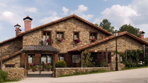 Un edificio de piedra con techo de paja, entrada, varias ventanas y jardineras florales.