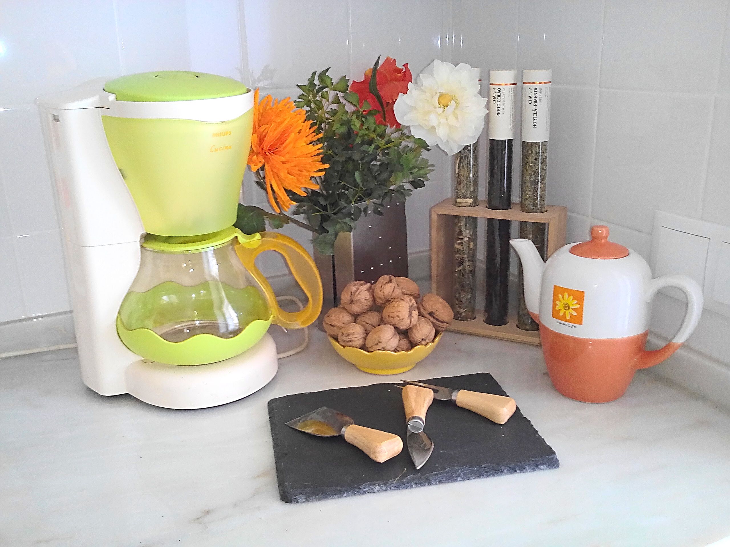 A kitchen counter with a coffee maker, a bowl of walnuts, a flower vase, and a knife block.