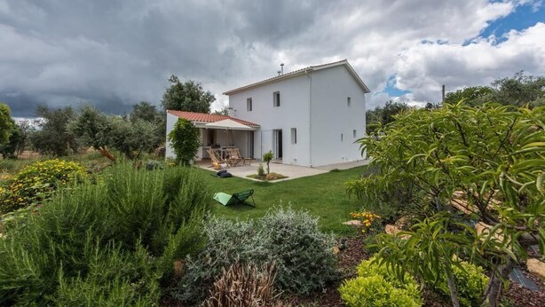 A modern two-story house with a red-tiled roof, surrounded by a well-maintained garden with various plants and a lawn. - Casa do Olival, Guest accommodation in Figueiró dos Vinhos. (Figueiró dos Vinhos)