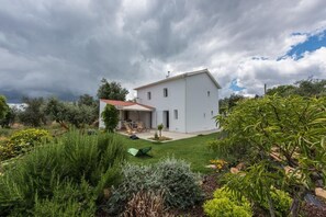 Ein modernes, zweistöckiges Haus mit rotem Ziegeldach, umgeben von einem gepflegten Garten mit verschiedenen Pflanzen und einer Rasenfläche.