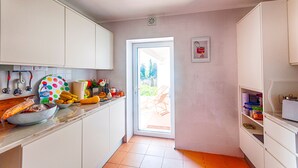 A kitchen with white cabinets, a countertop with various items, and a door leading to a patio area. - Casa do Olival, Guest accommodation in Figueiró dos Vinhos. (Figueiró dos Vinhos)