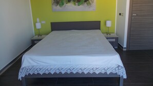 A bedroom with a bed, two bedside tables, a nightstand, a door, and a wall-mounted painting. - Apartment "Luna Nuova" (Tusa)