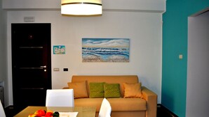 A room with a beige sofa, a painting of a beach scene, a teal accent wall, and a door with a light switch. - Apartment "Luna Nuova" (Tusa)