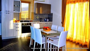A modern kitchen with white cabinets, a dining table with chairs, and a fruit basket. - Apartment "Luna Nuova" (Tusa)