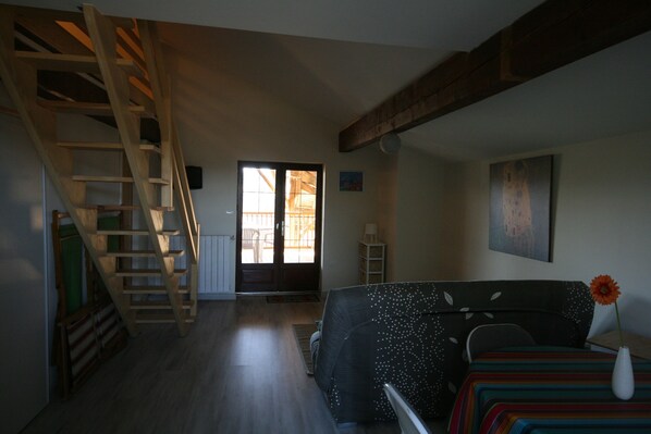 Une pièce avec un escalier en bois, un canapé recouvert d’une couverture colorée, un vase avec une fleur et un tableau accroché au mur.