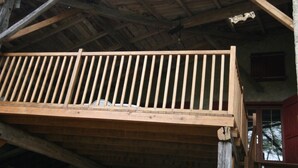 A rustic wooden building with a balcony, a bench, and a staircase leading to an upper level.