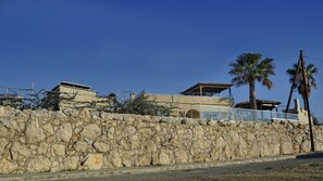 A stone wall with a building on top, a palm tree, and a clear blue sky.