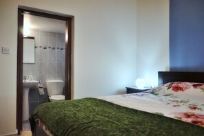 A bedroom with a bed, a nightstand, a lamp, and a view of the bathroom.