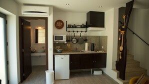 Cocina compacta con microondas, lavamanos y refrigerador. Se observa una escalera con un diseño singular a la derecha.