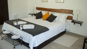 Una cama bien hecha con almohadas, una mesita de noche con una lámpara y un zapatero con zapatos blancos.