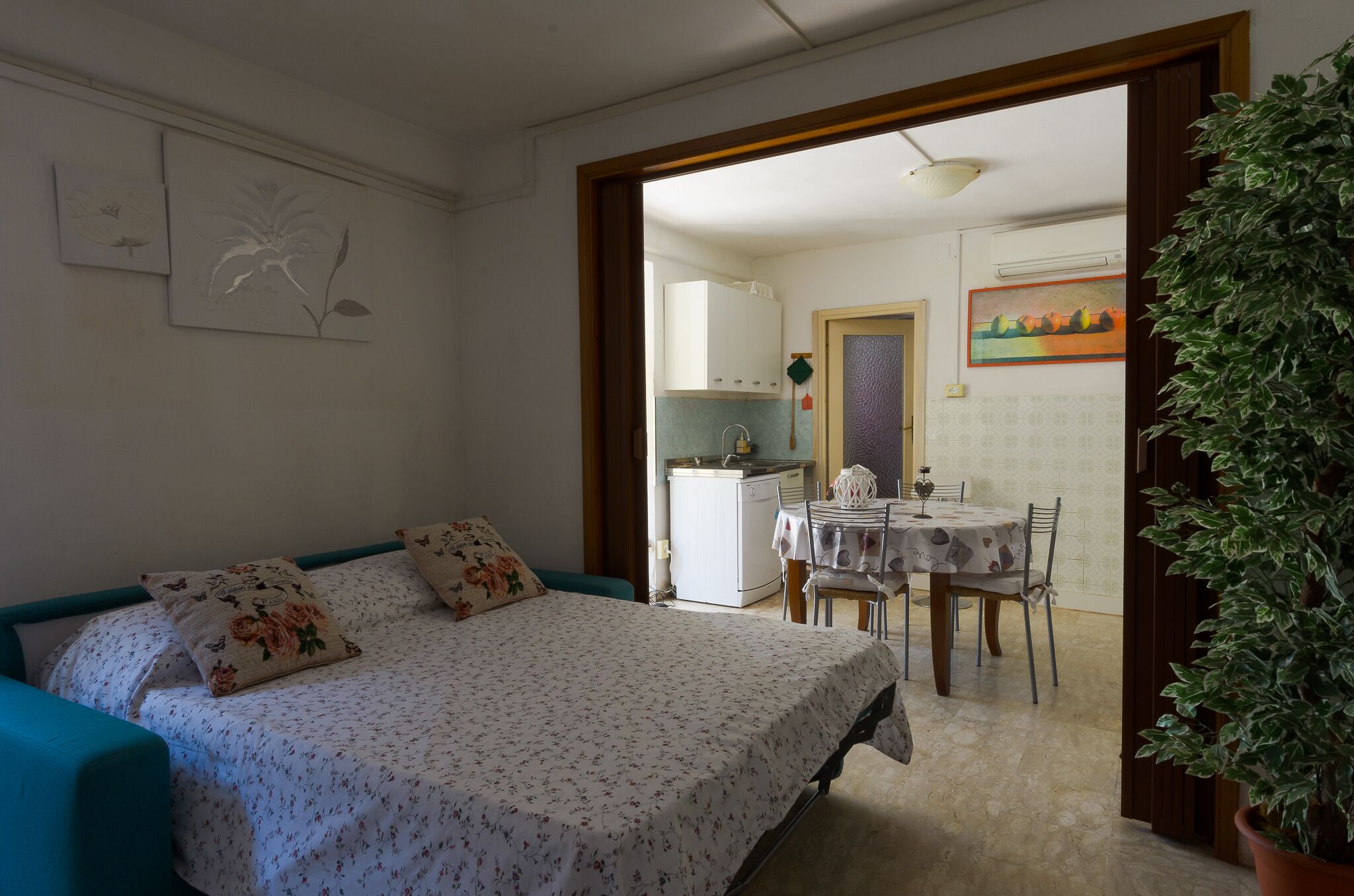 Une chambre à coucher avec un lit, un bureau et une chaise. On y trouve une plante en pot et un tableau accroché au mur.