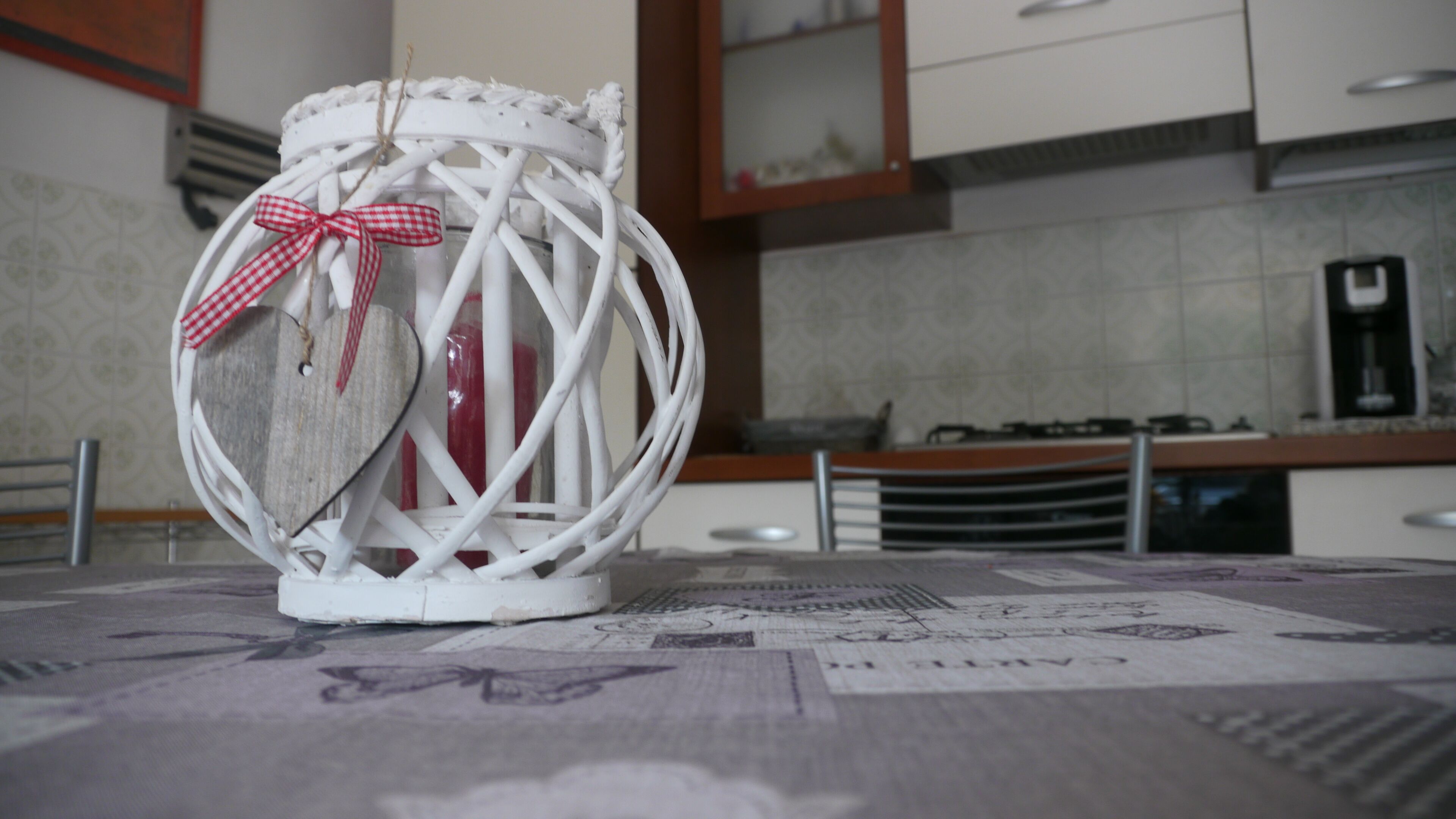 A white lantern with a red and white checkered ribbon on a table with a newspaper pattern.