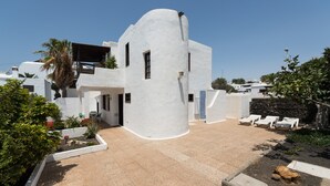 Un bâtiment moderne aux murs blancs, doté d’une façade incurvée, d’un patio aménagé avec des fauteuils et d’un petit jardin.