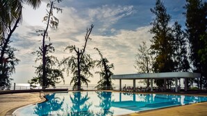 A swimming pool with a clear blue water, surrounded by trees and a covered area with lounge chairs. - Cozy Beachfront Condo With Jacuzzi On Balcony (Tambon Cha-am)