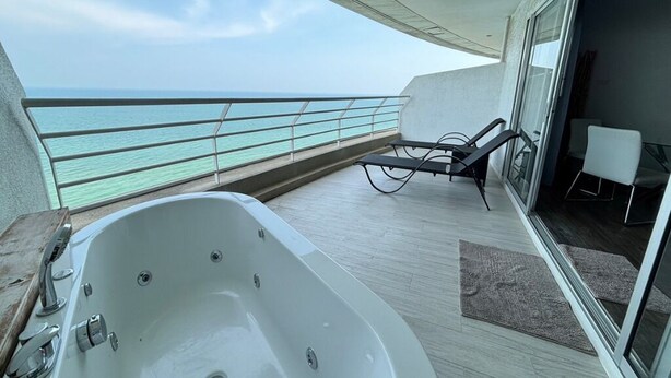 A balcony with a view of the sea, a jacuzzi, and a seating area with a table and chairs. - Cozy Beachfront Condo With Jacuzzi On Balcony (Tambon Cha-am)