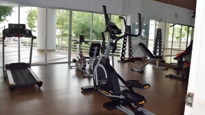 A gym with cardio machines, weight stations, and a large window offering a view of the outdoors. - Cozy Beachfront Condo With Jacuzzi On Balcony (Tambon Cha-am)