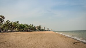 A beach with palm trees and buildings in the background. - Cozy Beachfront Condo With Jacuzzi On Balcony (Tambon Cha-am)