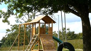 A wooden play structure with a slide and climbing wall, surrounded by grass and trees. - SPACIOUS Family Farmhouse in 3 ACRES with STUNNING VIEWS, EXCLUSIVE USE. (Sourdeval)