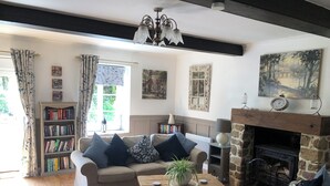 A cozy living room with a sofa, a coffee table, a fireplace, a bookshelf, and a window with curtains. - SPACIOUS Family Farmhouse in 3 ACRES with STUNNING VIEWS, EXCLUSIVE USE. (Sourdeval)