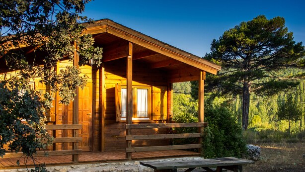 Une cabane en bois dotée d’une véranda, d’une table de pique-nique et de fondations en pierre.