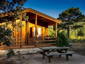 A wooden cabin with a porch, a picnic table, and a stone foundation. - Cabins El Llano de los Conejos - Cabin 11 (Cañamares)