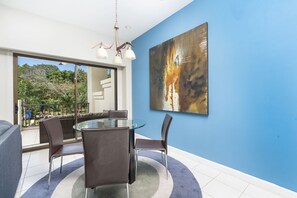 A modern dining area with a glass table and chairs, a blue accent wall, and a large abstract painting.