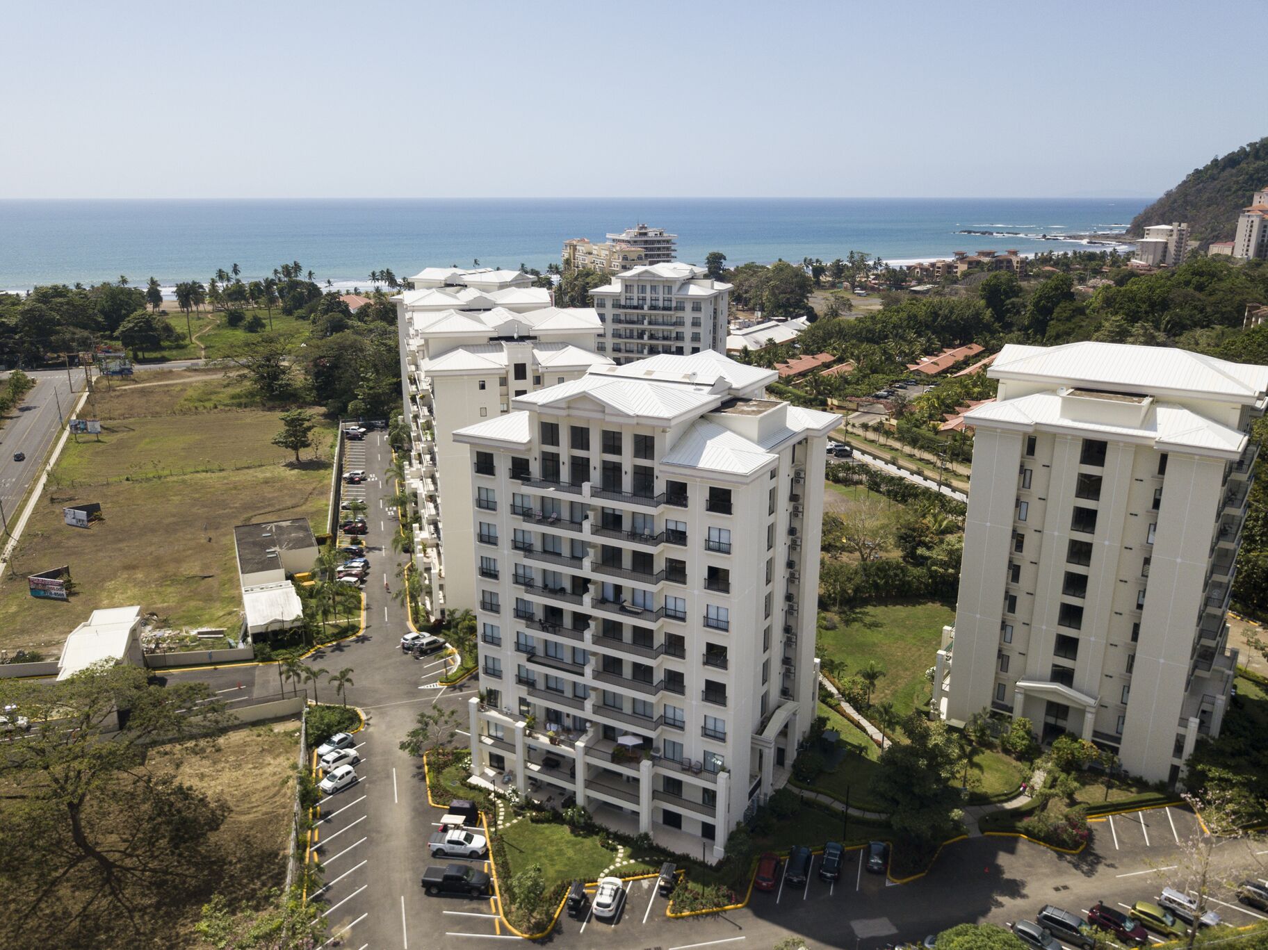 Een hoog appartementencomplex met meerdere balkons, een parkeerplaats en uitzicht op de oceaan.
