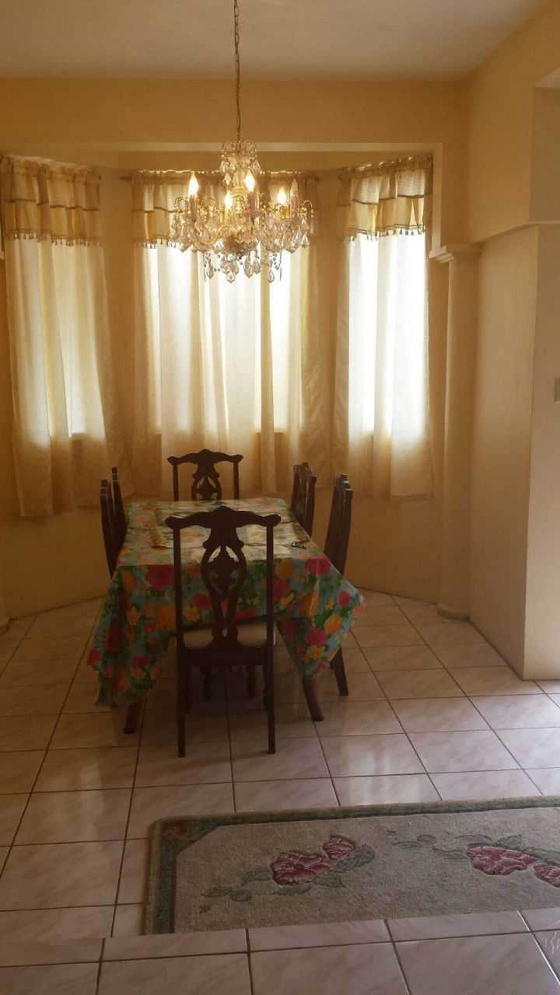 Zona de menjador amb un penjallum, cortines i un mantell de taula amb motius florals.