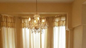 A dining area with a chandelier, curtains, and a floral tablecloth.