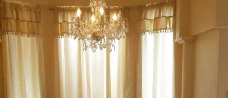 Zona de menjador amb un penjallum, cortines i un mantell de taula amb motius florals.