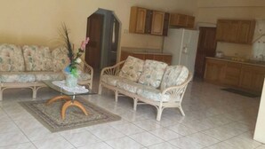 A living room with a sofa, a coffee table, and a decorative vase. There is a kitchen area with wooden cabinets and a refrigerator.