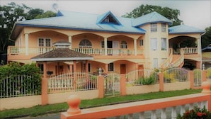 A large, two-story house with a blue roof, multiple balconies, and a white fence.