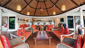 A spacious living area with wicker furniture, a central coffee table, and a thatched roof ceiling.